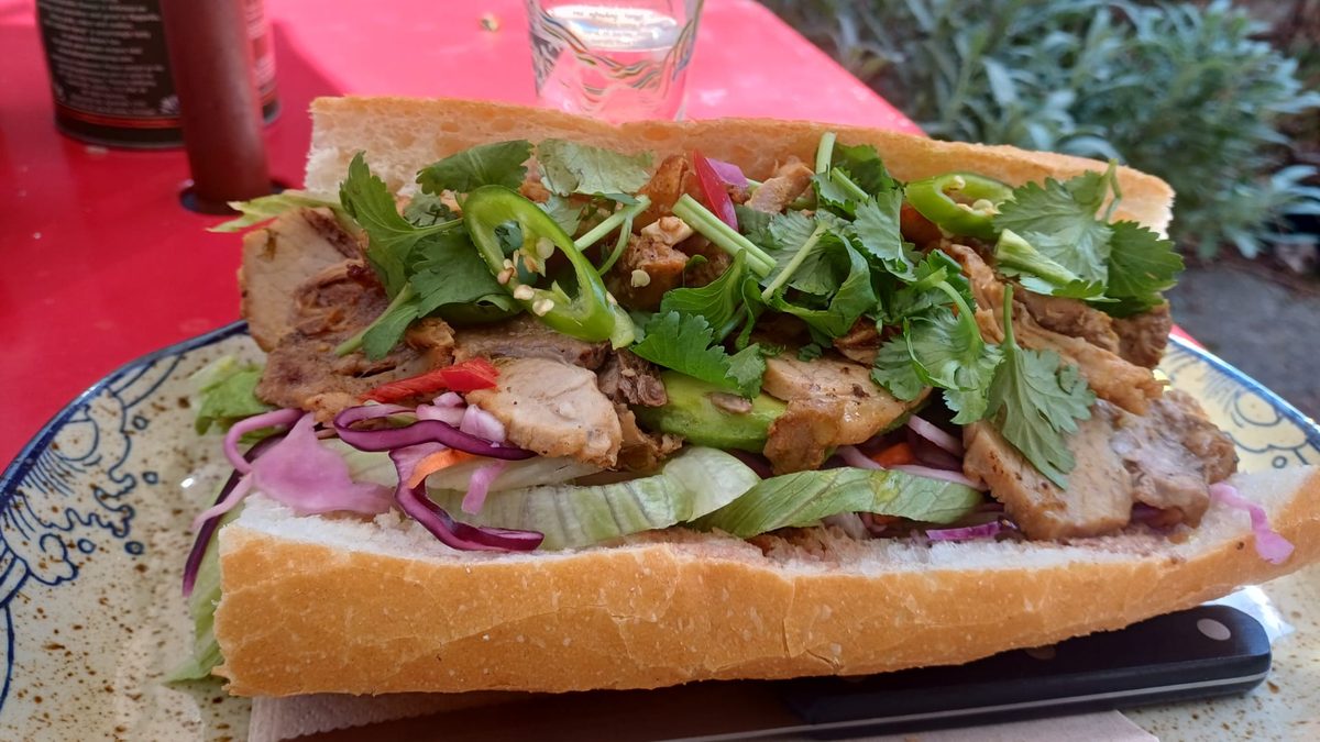 A bánh mì on a patterned plate on a red table outside the shop.