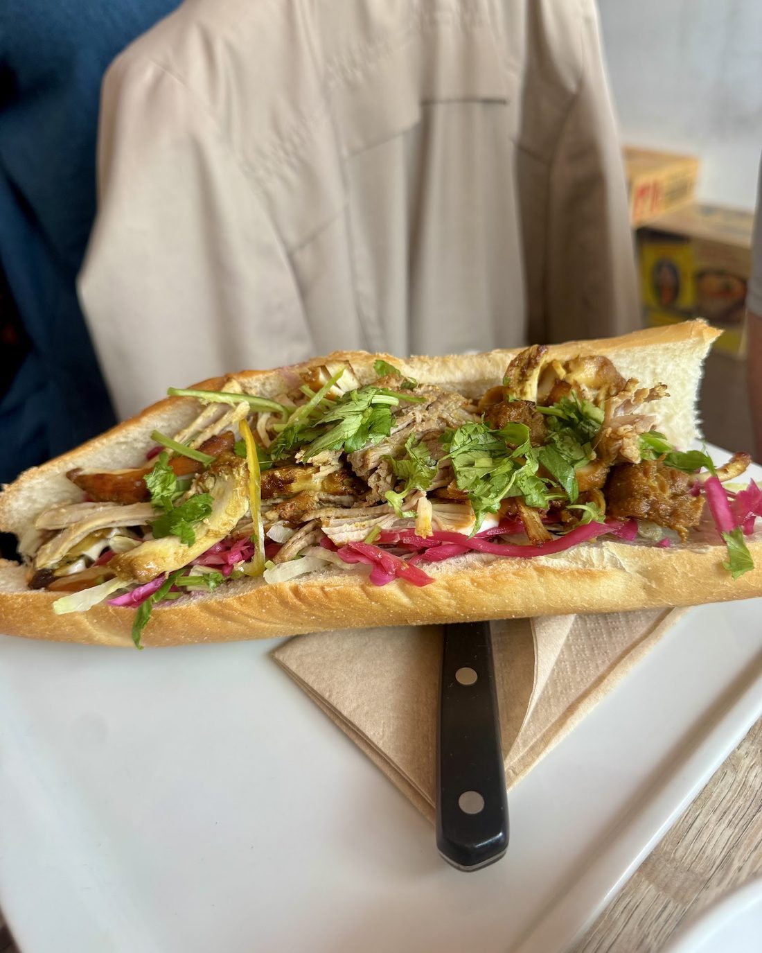 A bánh mì baguette filled with pulled pork, pickled red cabbage, spring onion and coriander, on a board.