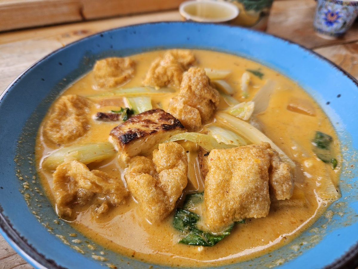 A blue bowl of yellow Thai curry with fried tofu and lemongrass.