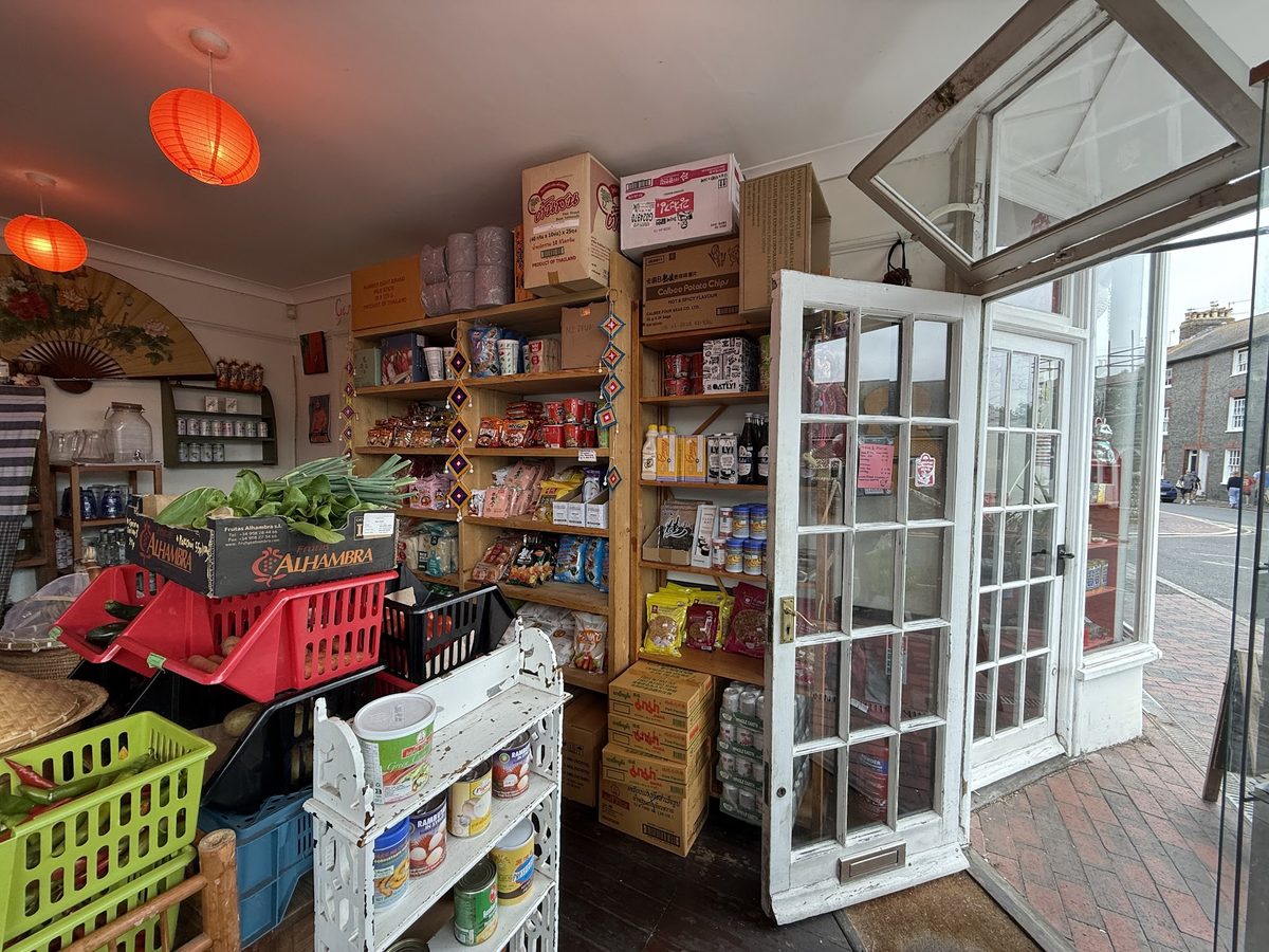 Shelves of Asian groceries in tins, jars and packets, with crates of fresh produce by the open shop door.
