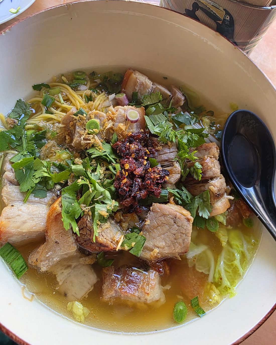 A wide bowl of noodle soup topped with crisp pork belly, chilli oil, coriander and spring greens.